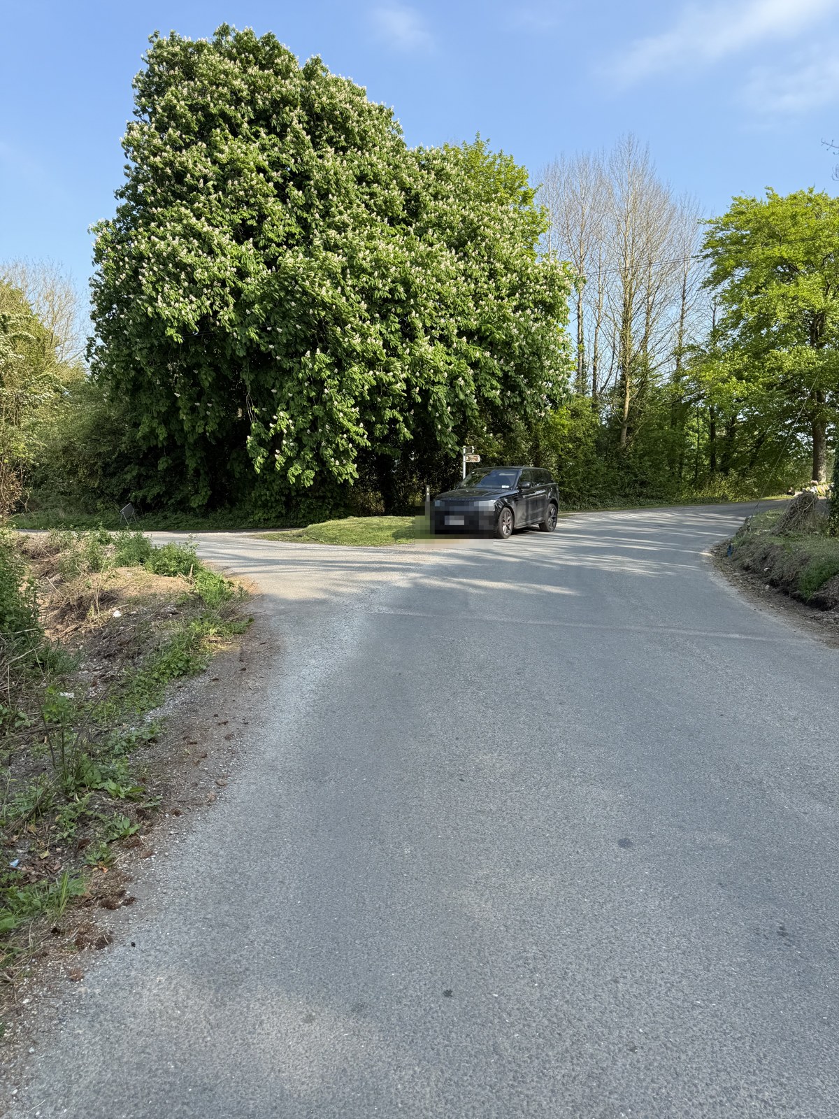 The same approach junction on 1 May 2025, the left verge cut back to bare soil and ground disturbed along the edge